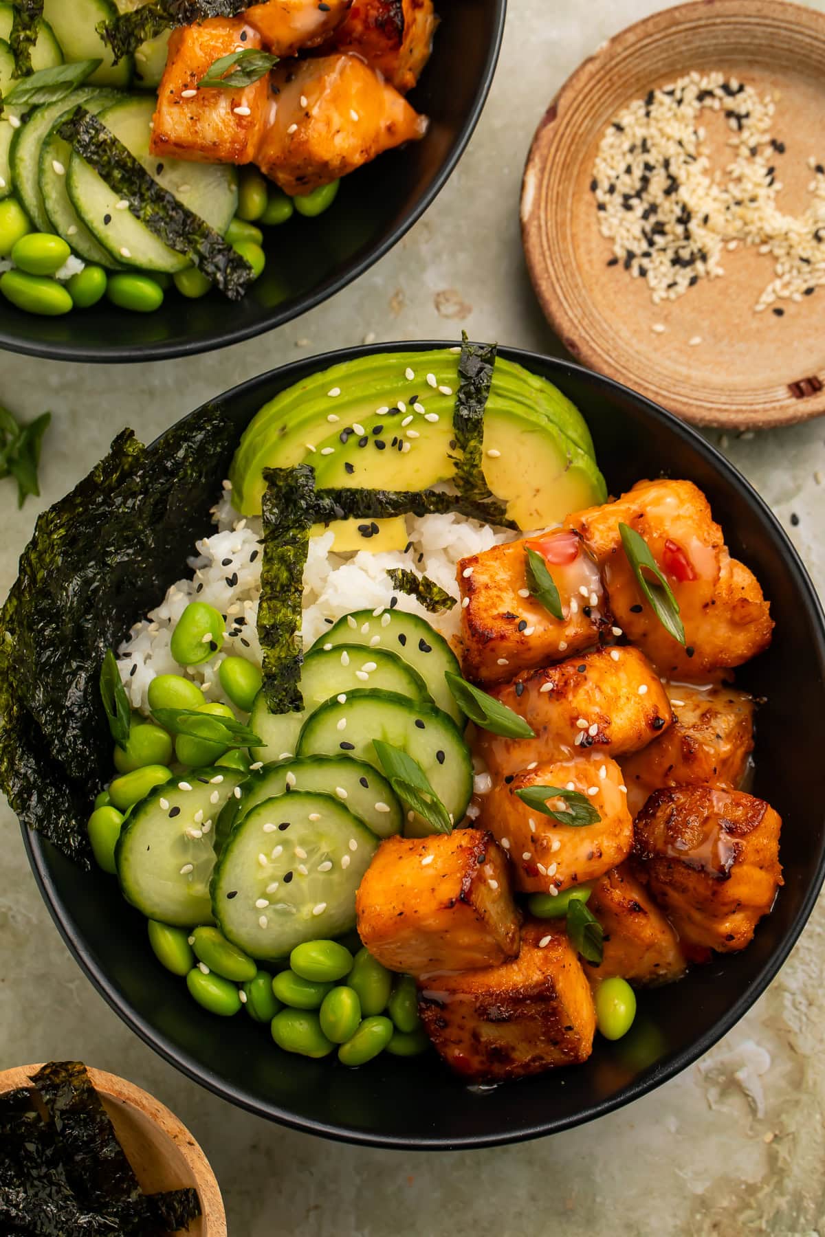 Overhead photo of a bang bang salmon bowl with rice, avocado, cucumber, edamame, and seaweed