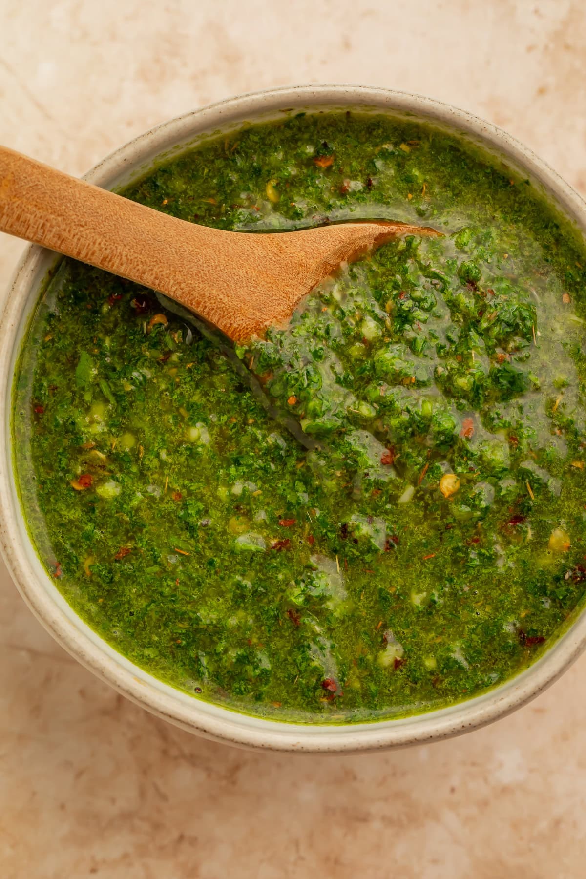 Overhead image of a bowl of chimichurri sauce with a wooden spoon resting inside.