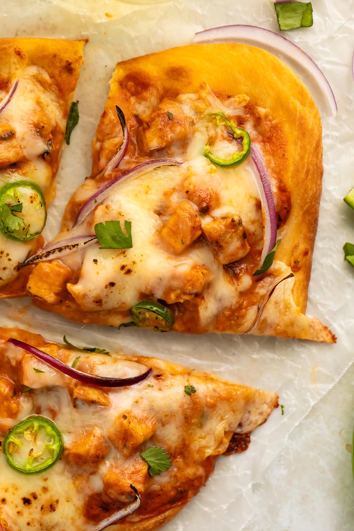 Close up of a slice of chicken tikka masala pizza topped with melted cheese, sliced jalapeños and red onion.