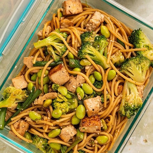 Noodle salad with tofu and green veg in a glass meal prep container.