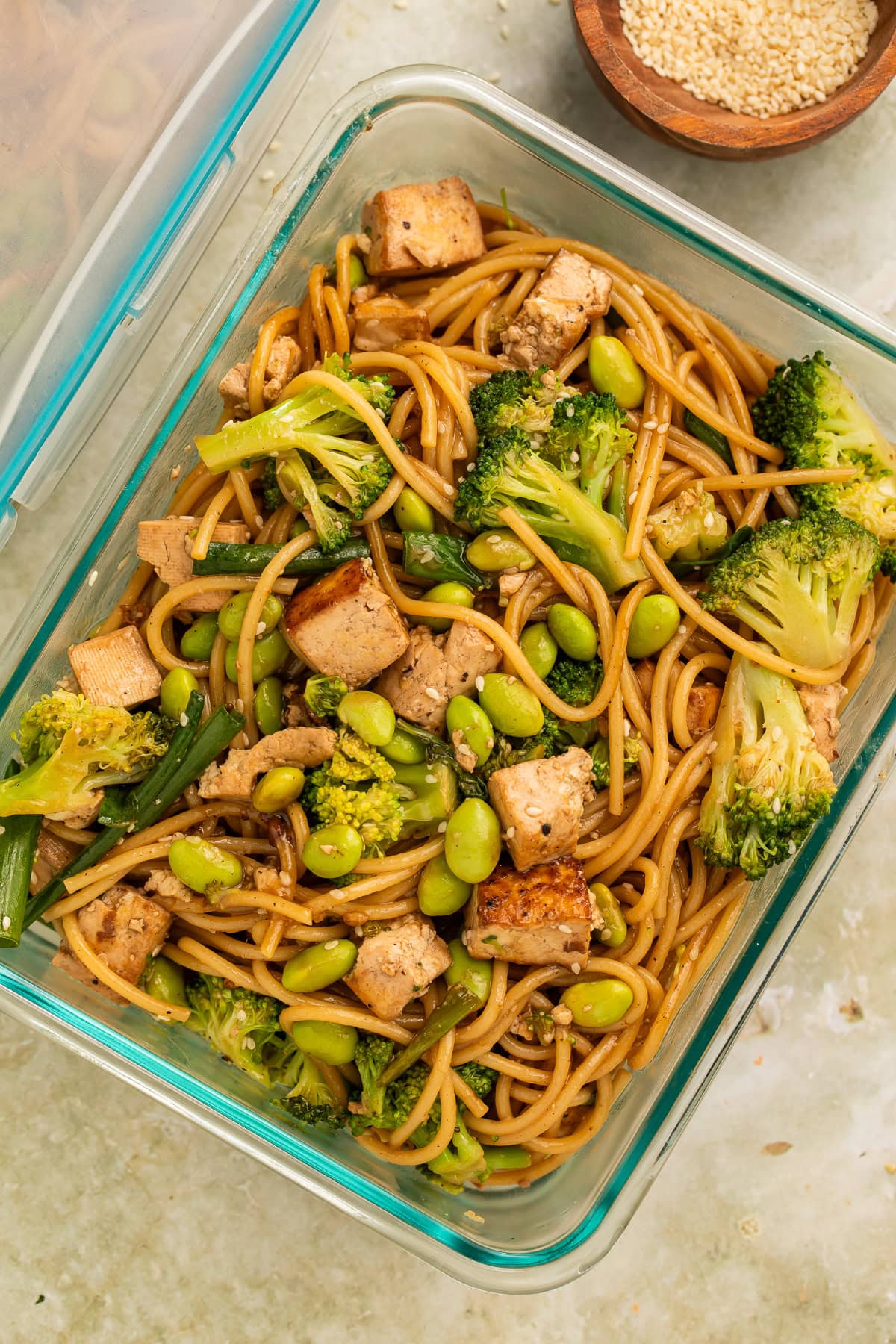 Noodle salad with tofu and green veg in a glass meal prep container.