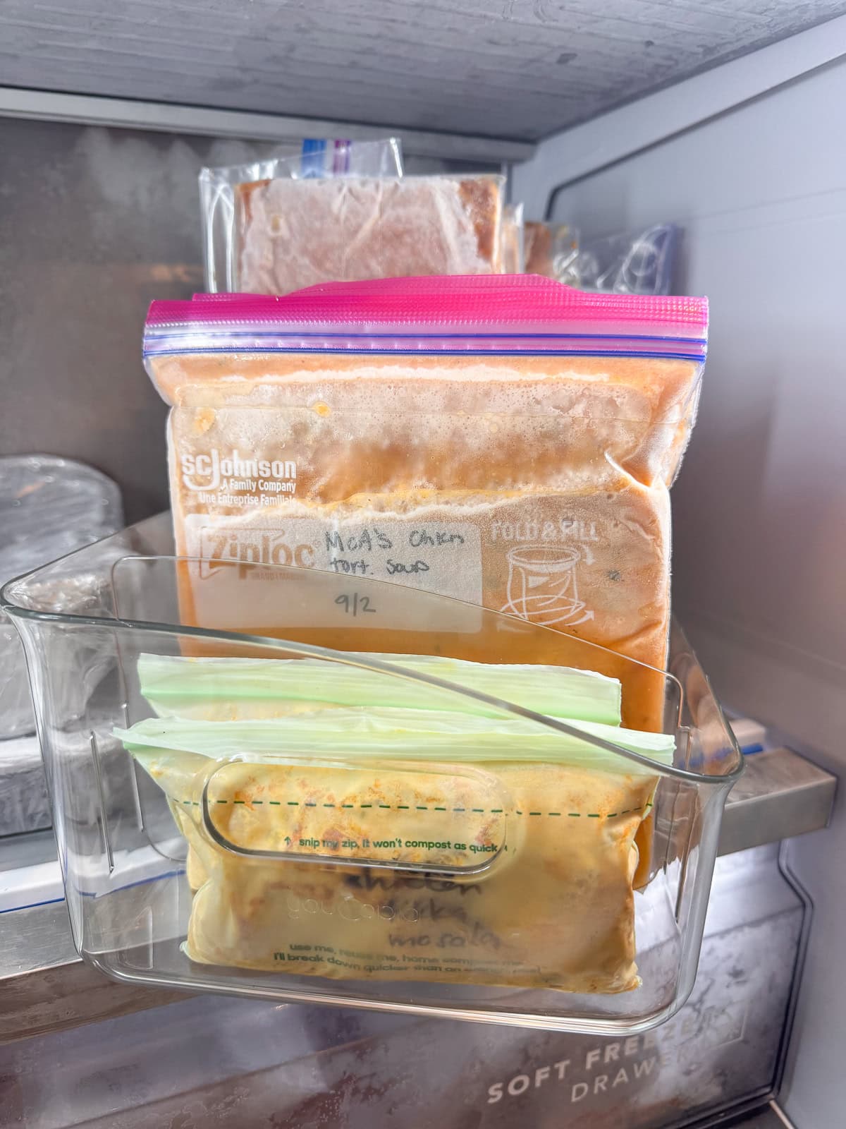 A freezer organization bin with labeled frozen meal bags stored upright in a freezer drawer