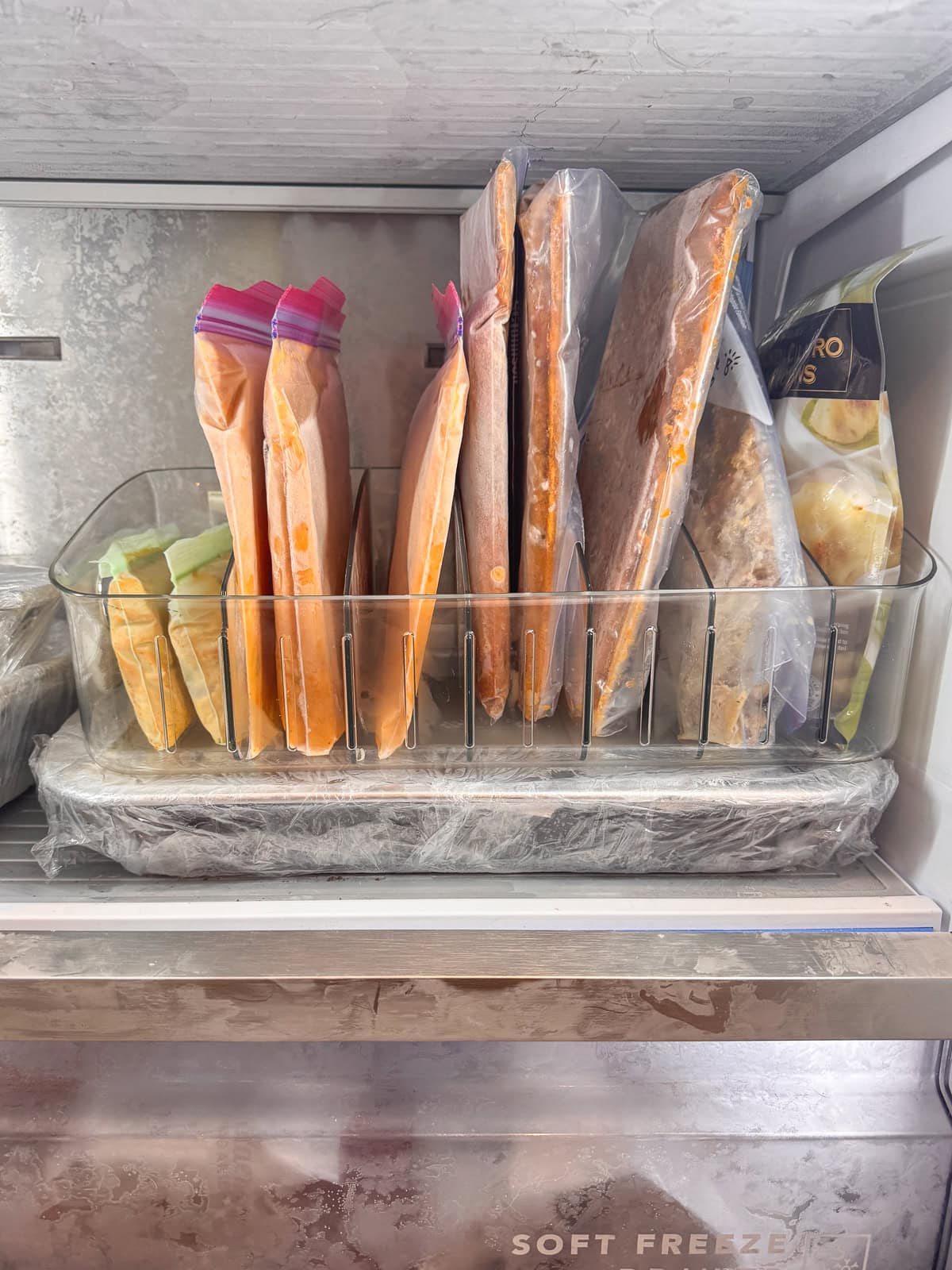 Side view of a freezer organization bin with frozen meals and sauces stored upright in labeled freezer bags