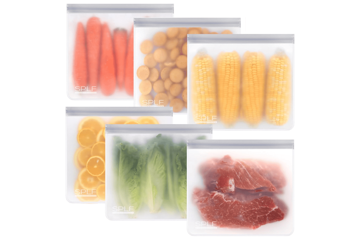 Reusable silicone freezer bags filled with vegetables, citrus, corn, lettuce, and meat displayed against a white background