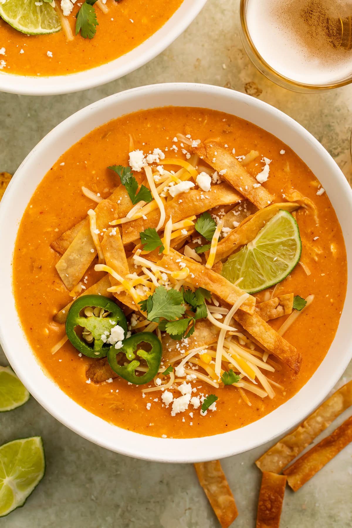 Creamy instant pot chicken enchilada soup topped with tortilla strips, shredded cheese, jalapeño slices, cilantro, and lime wedges