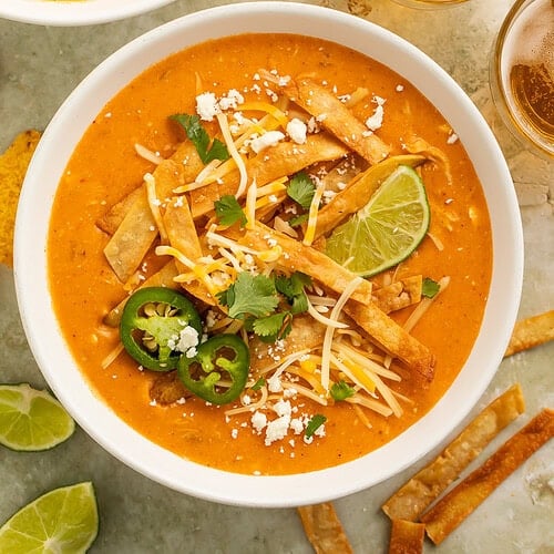 Instant pot chicken enchilada soup in white bowls topped with tortilla strips, cheese, jalapeños, cilantro, and lime