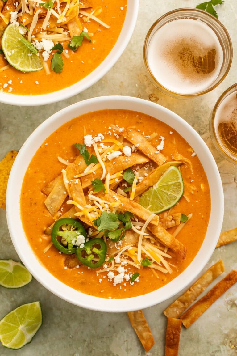 Instant pot chicken enchilada soup in white bowls topped with tortilla strips, cheese, jalapeños, cilantro, and lime
