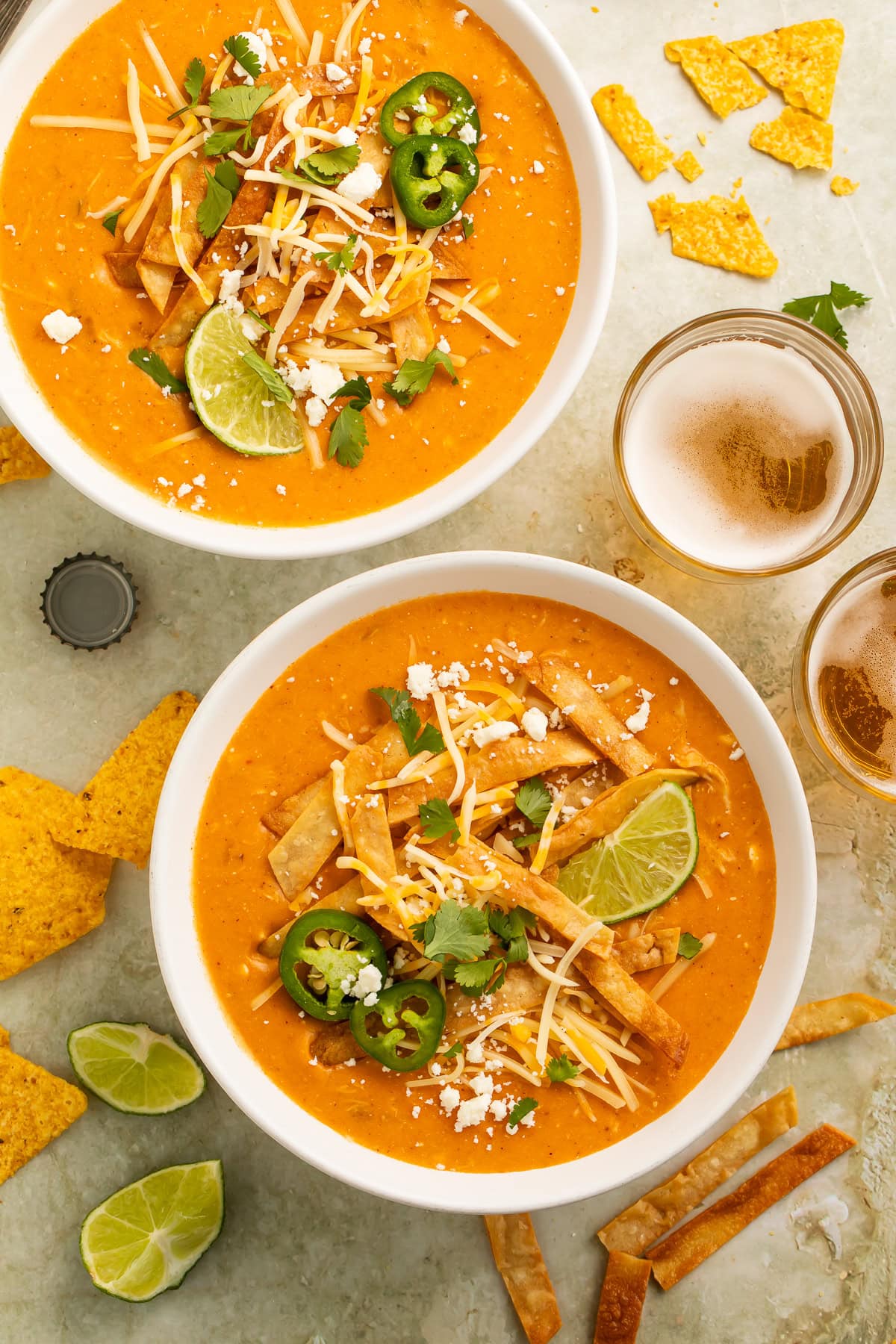 Overhead view of creamy chicken enchilada soup with tortilla strips, cheese, jalapeños, cilantro, and lime wedges