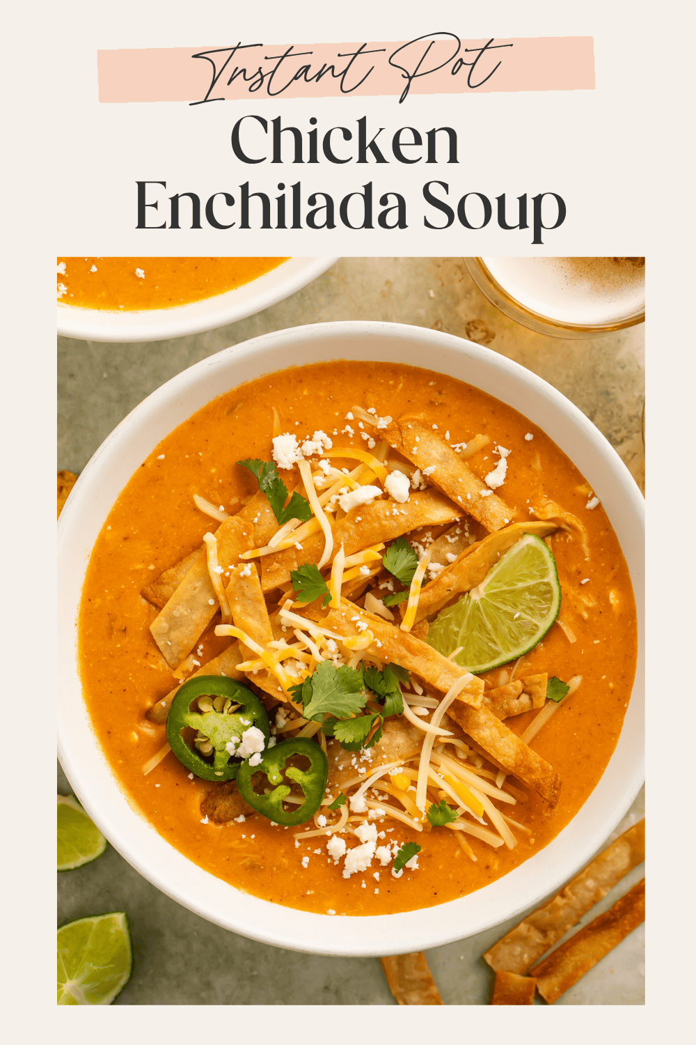 Overhead view of creamy chicken enchilada soup in white bowl with tortilla strips and lime