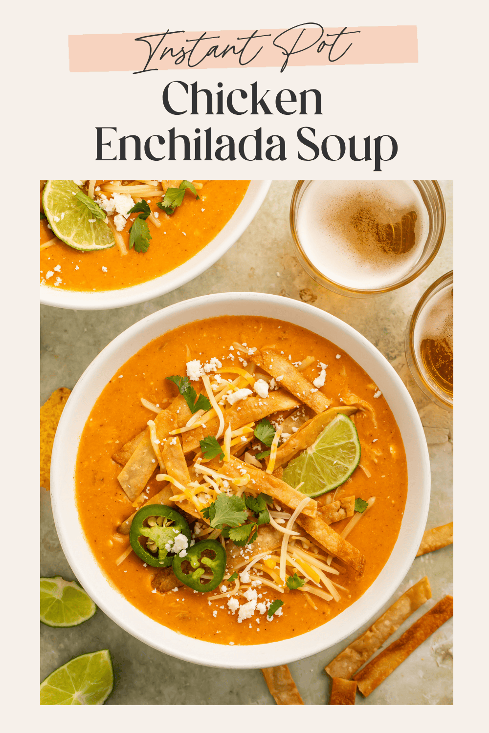 Two white bowls of chicken enchilada soup with tortilla strips, jalapeño, and lime wedges