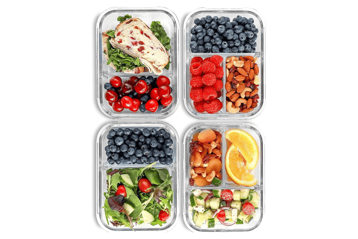 Compartmentalized glass meal prep containers filled with sandwiches, berries, nuts, salad, dried fruit, and fresh vegetables