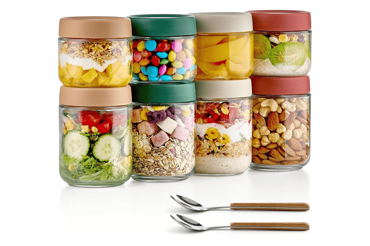 Glass storage jars with colorful lids filled with snacks, salads, overnight oats, fruit, and nuts