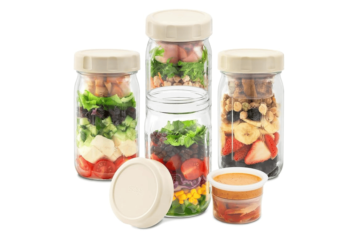 Glass salad jars layered with vegetables, greens, fruit, granola, and dressing containers