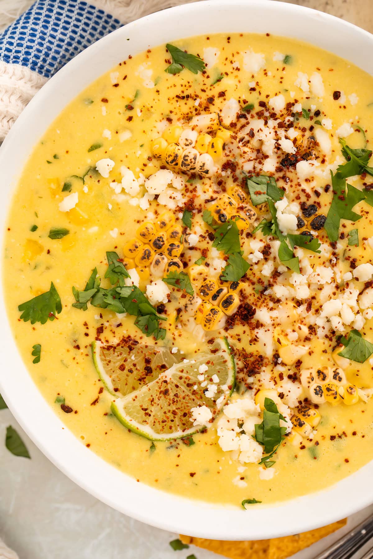 Close up of a bowl of creamy corn soup topped with cilantro, charred corn, cojita, lime slices and Tajin.
