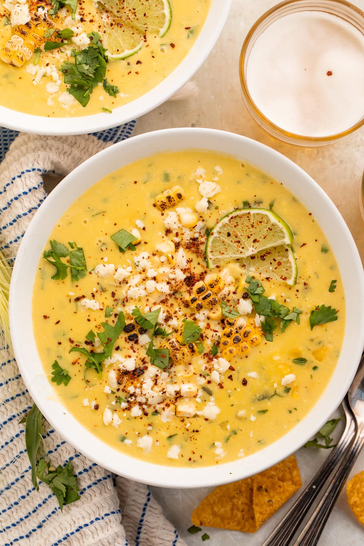 White bowls of creamy yellow Mexican corn soup topped with chili powder, lime slices, cojita and cilantro.