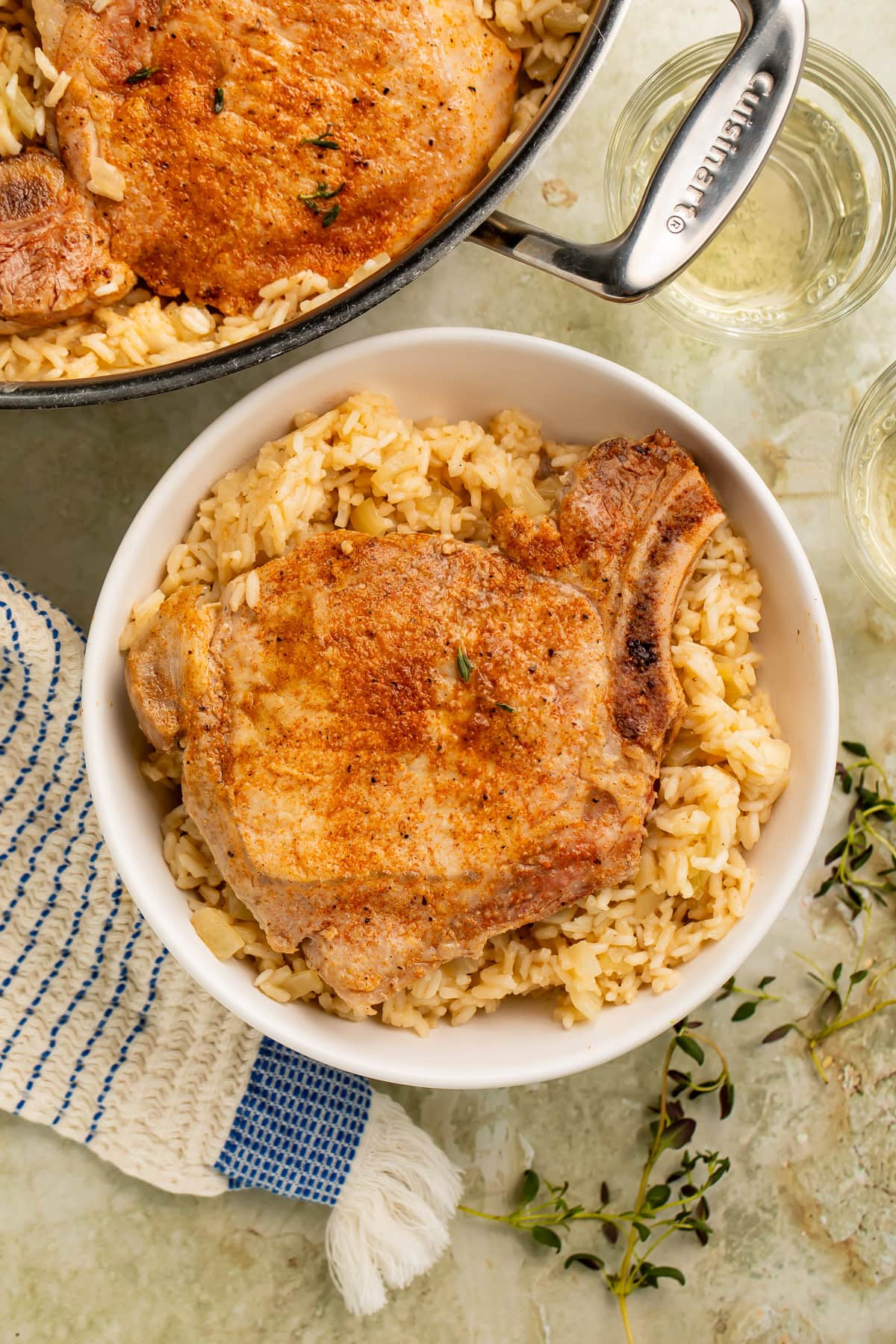Bone-in pork chop served over seasoned rice in a white bowl with skillet in background