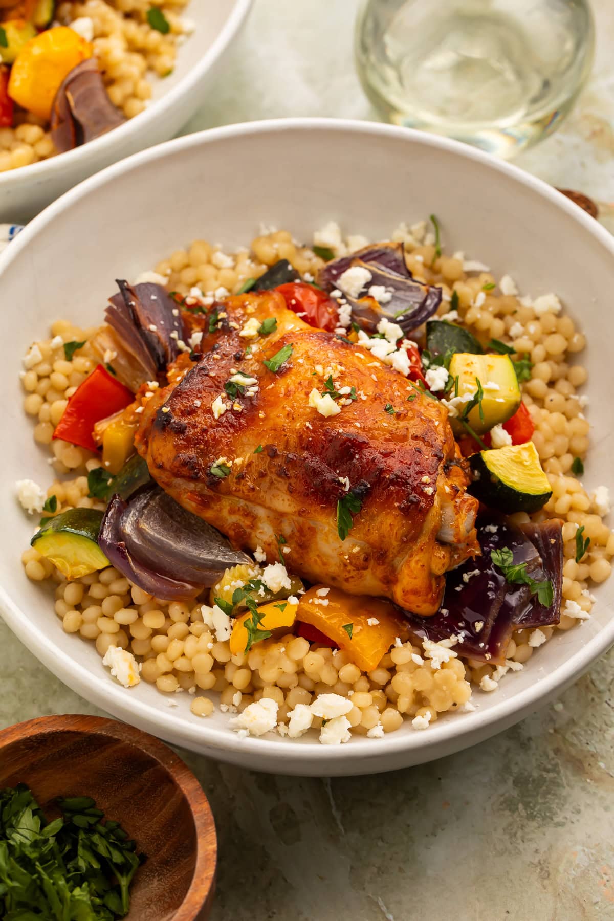 Side on image of a chicken thigh with roasted vegetables sitting on a bed of couscous and feta.