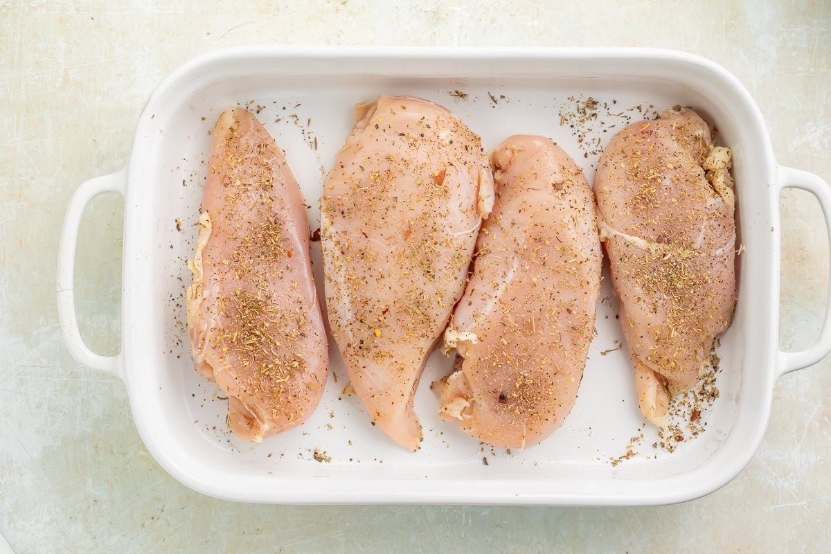 Seasoned chicken breasts in a white baking dish.