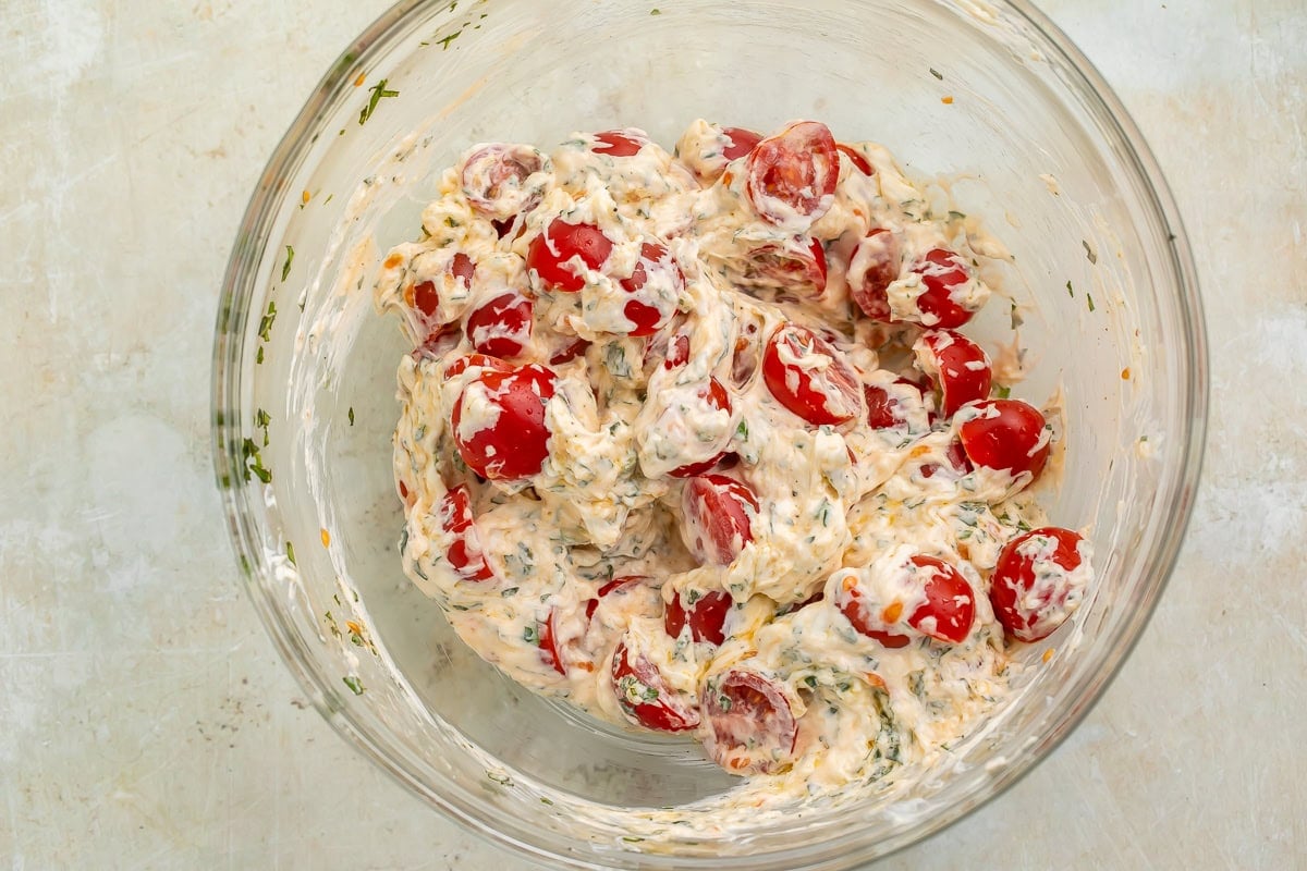 Cherry tomatoes stirred into a creamy sauce in a glass bowl.