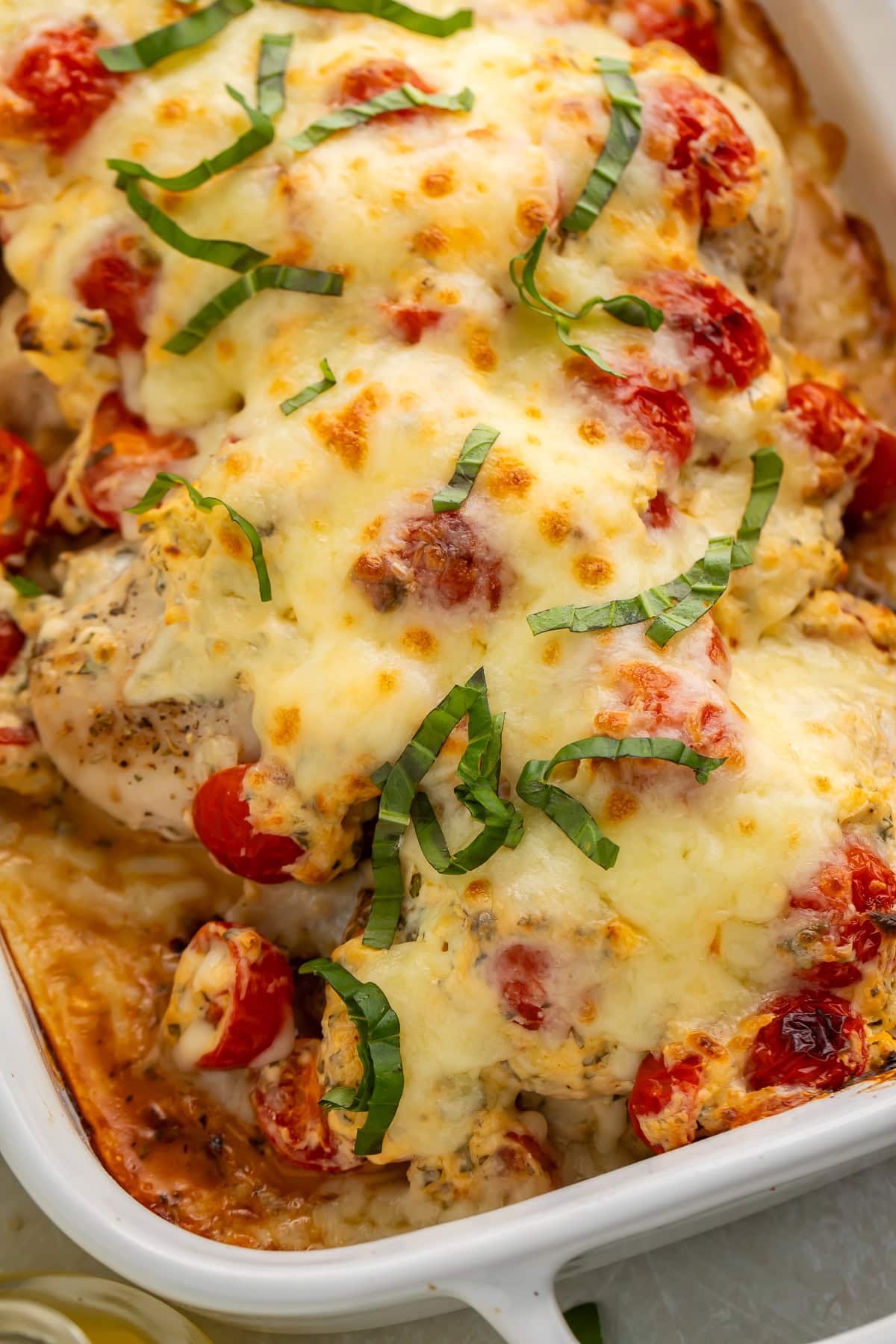 Close up of bruschetta chicken topped with melted cheese and shredded basil in a white serving dish.