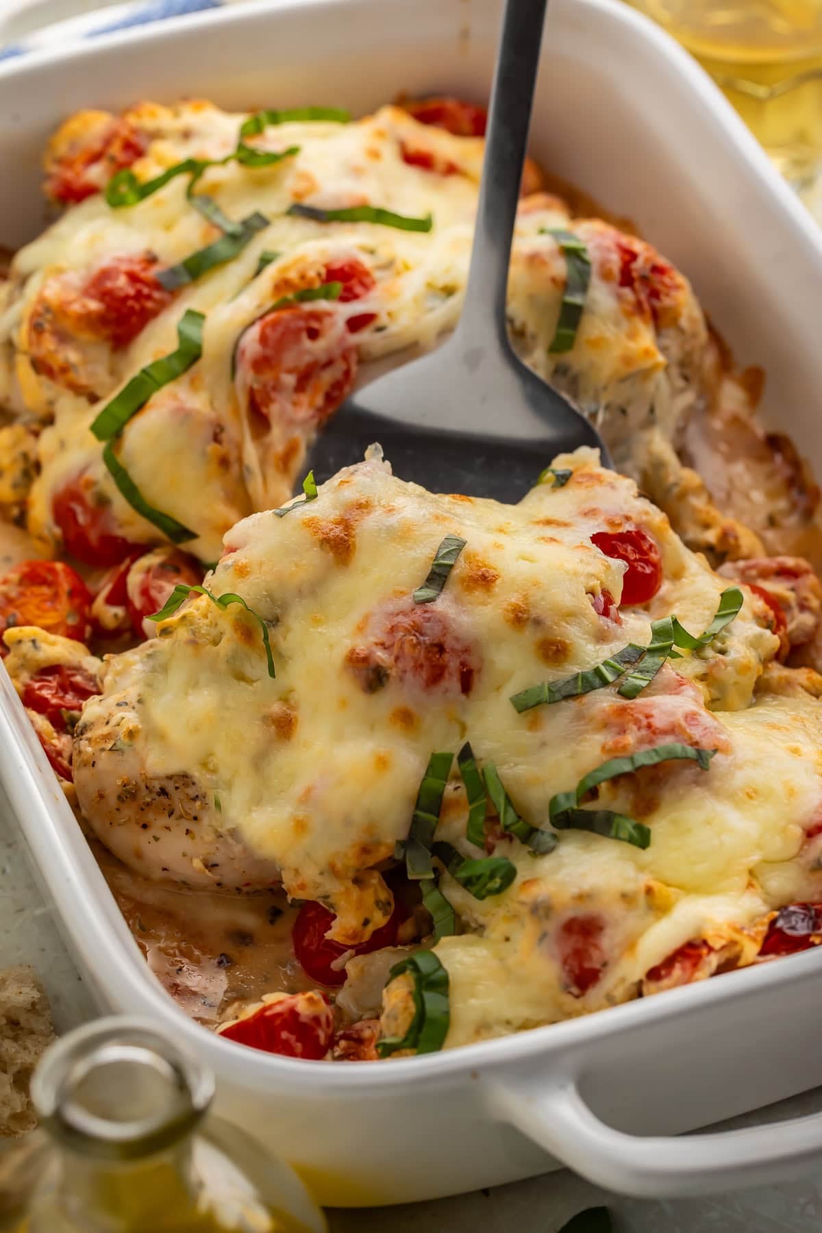 A black spatula lifting a baked bruschetta chicken breast out of a baking dish.