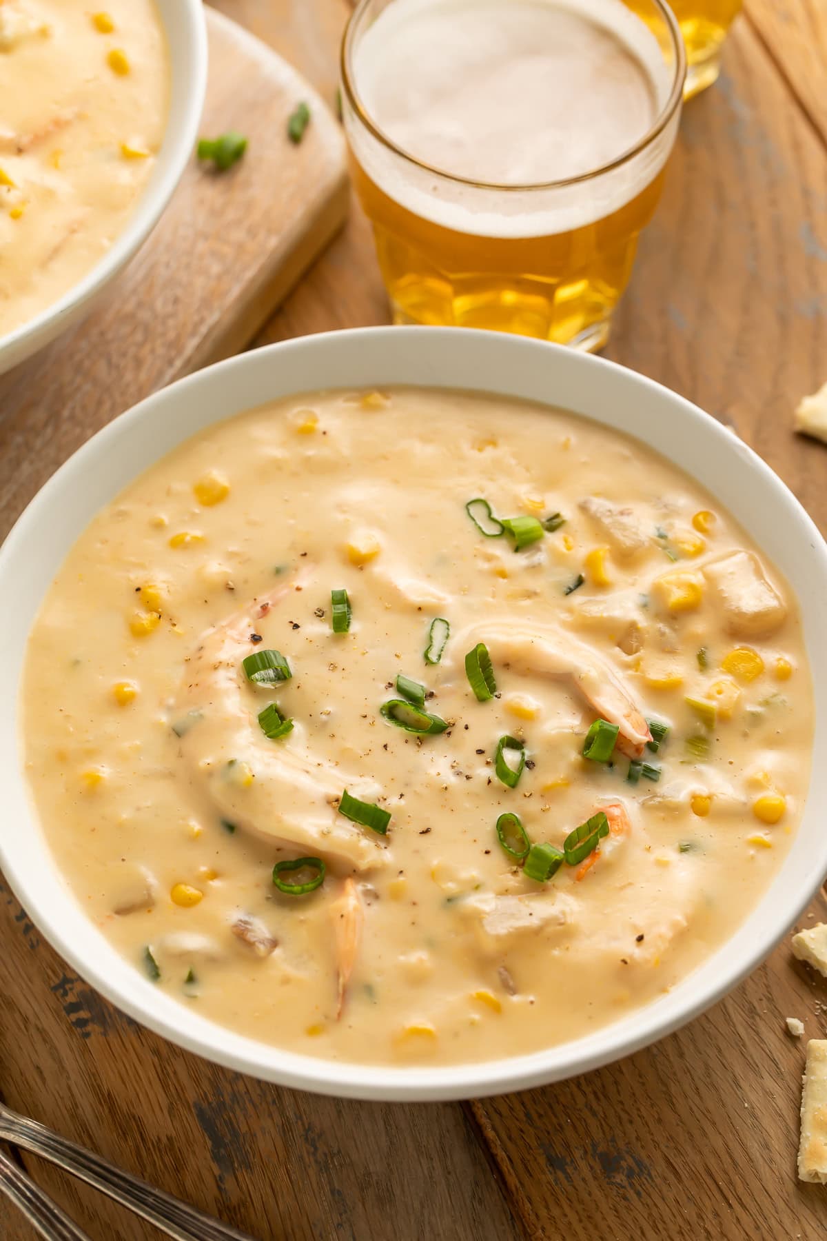 Side on view of a bowl of creamy corn and shrimp chowder with a glass of beer in the background.