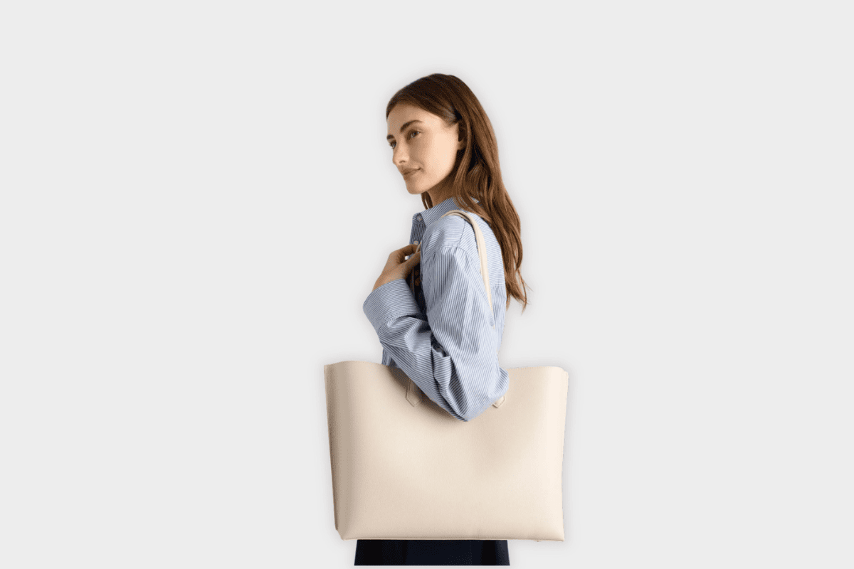 Woman carrying Quince soft ivory Italian leather triple compartment shopper tote over shoulder