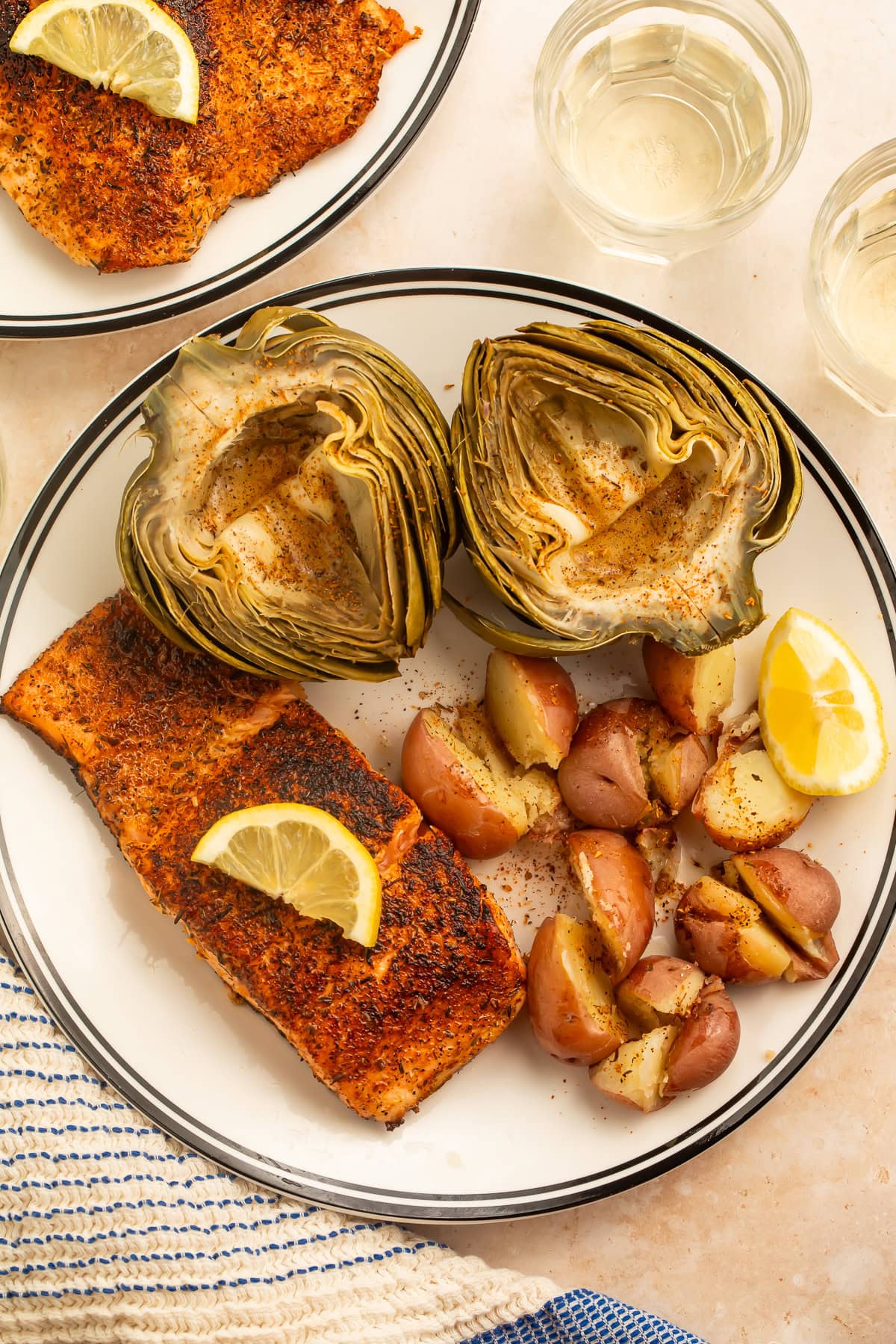 Plate of steamed artichokes, red potatoes and spiced salmon served with lemon wedges and butter.