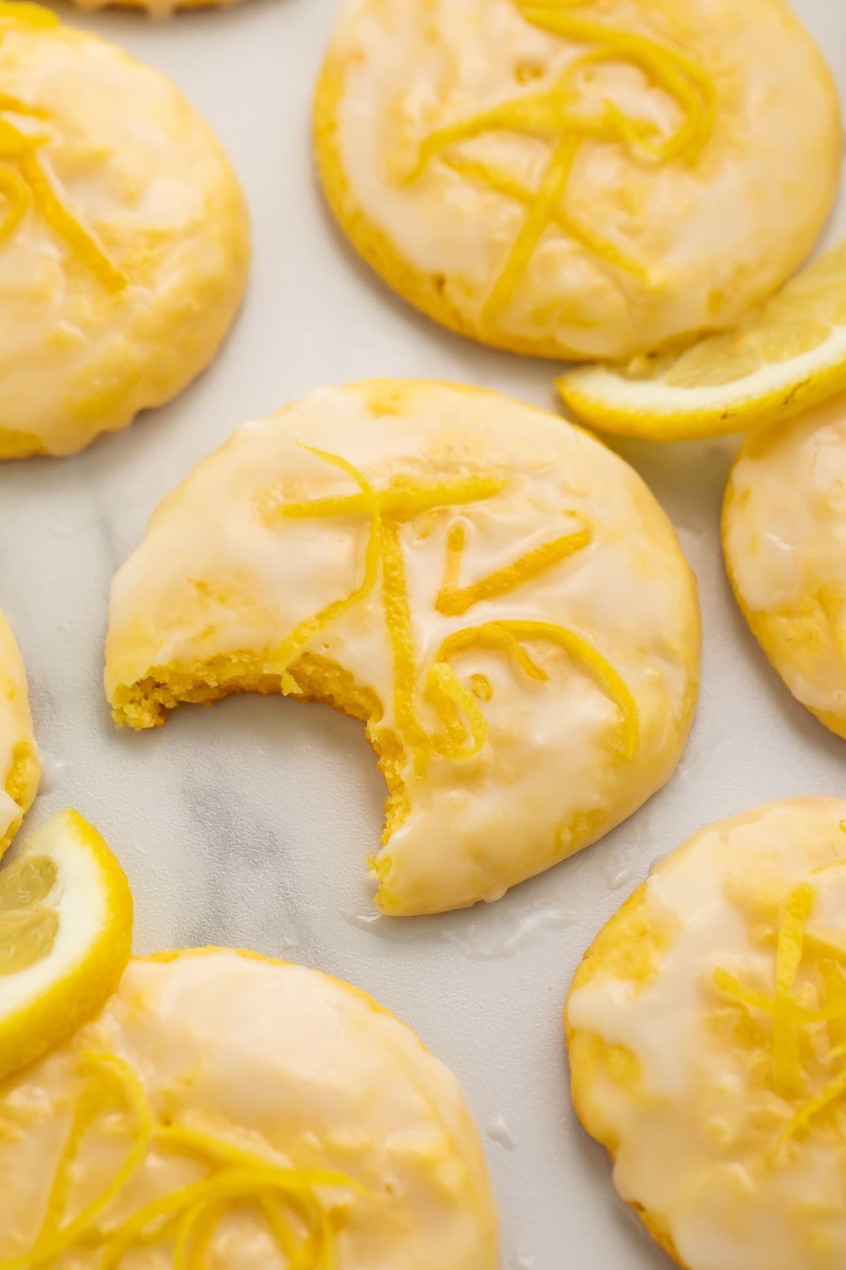 Close up of frosted lemon cookies. The middle cookie has a bite taken out of it.