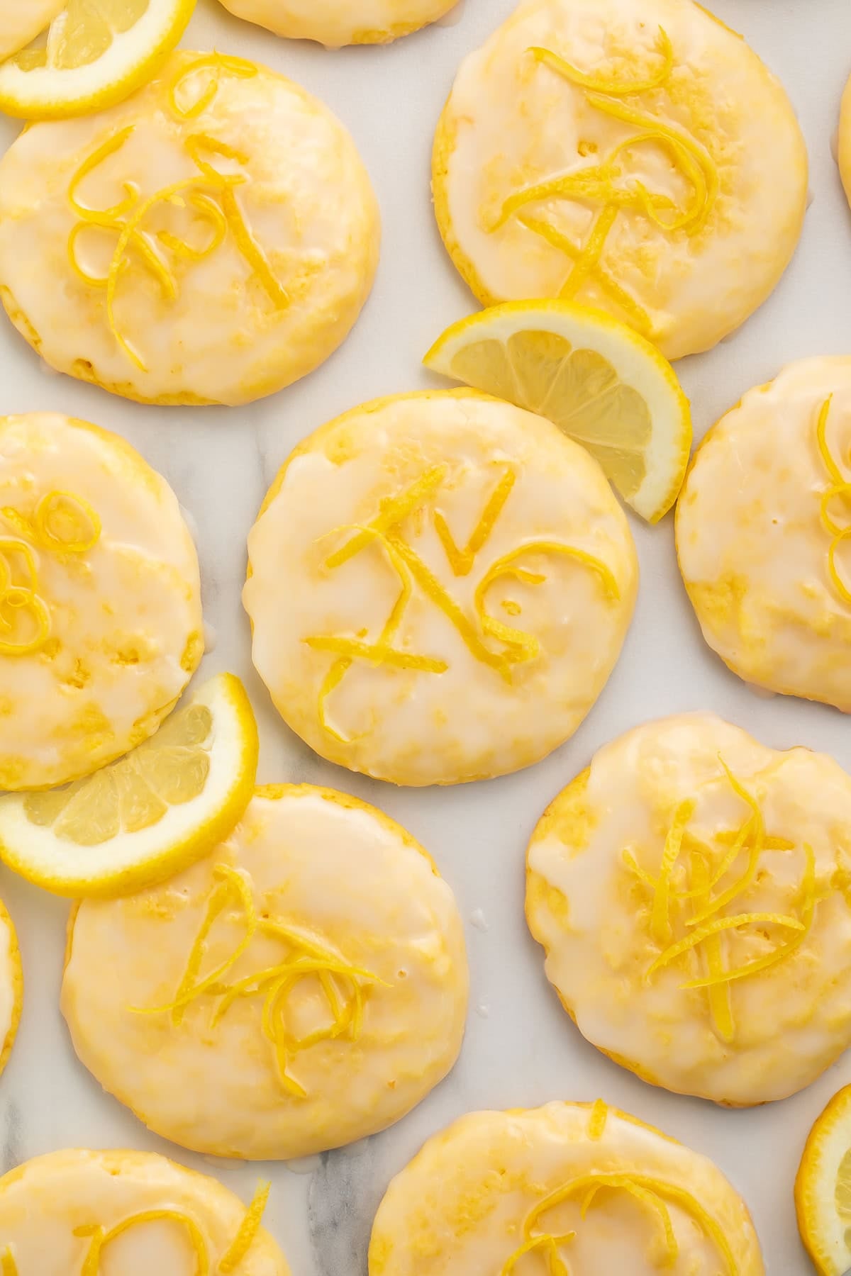 Frosted lemon cookies and lemon slices on a piece of white baking parchment.