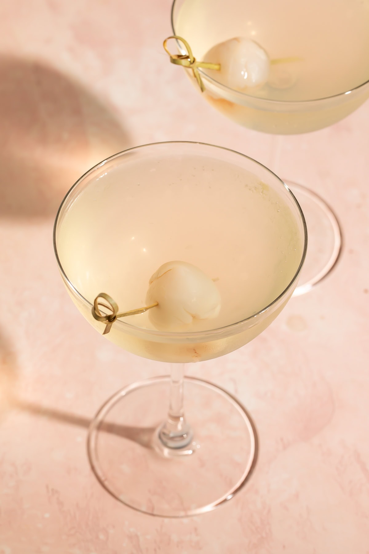 Close up of a lychee martini garnished with a lychee on a cocktail skewer.