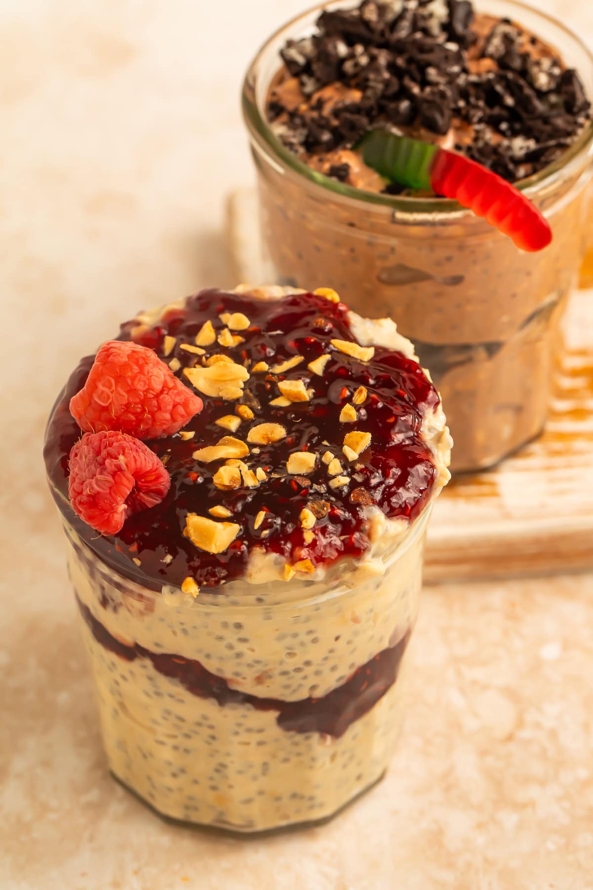 wo yogurt parfait jars, one layered with berry compote and raspberries and the other layered with chocolate cookie pieces and topped with a gummy worm