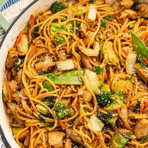 Close up of a skillet of saucy noodles with chopped cooked chicken and vegetables.
