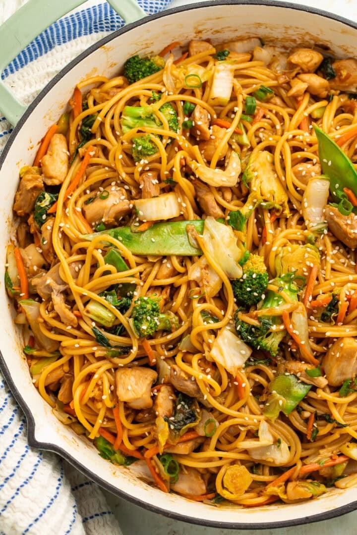 Close up of a skillet of saucy noodles with chopped cooked chicken and vegetables.