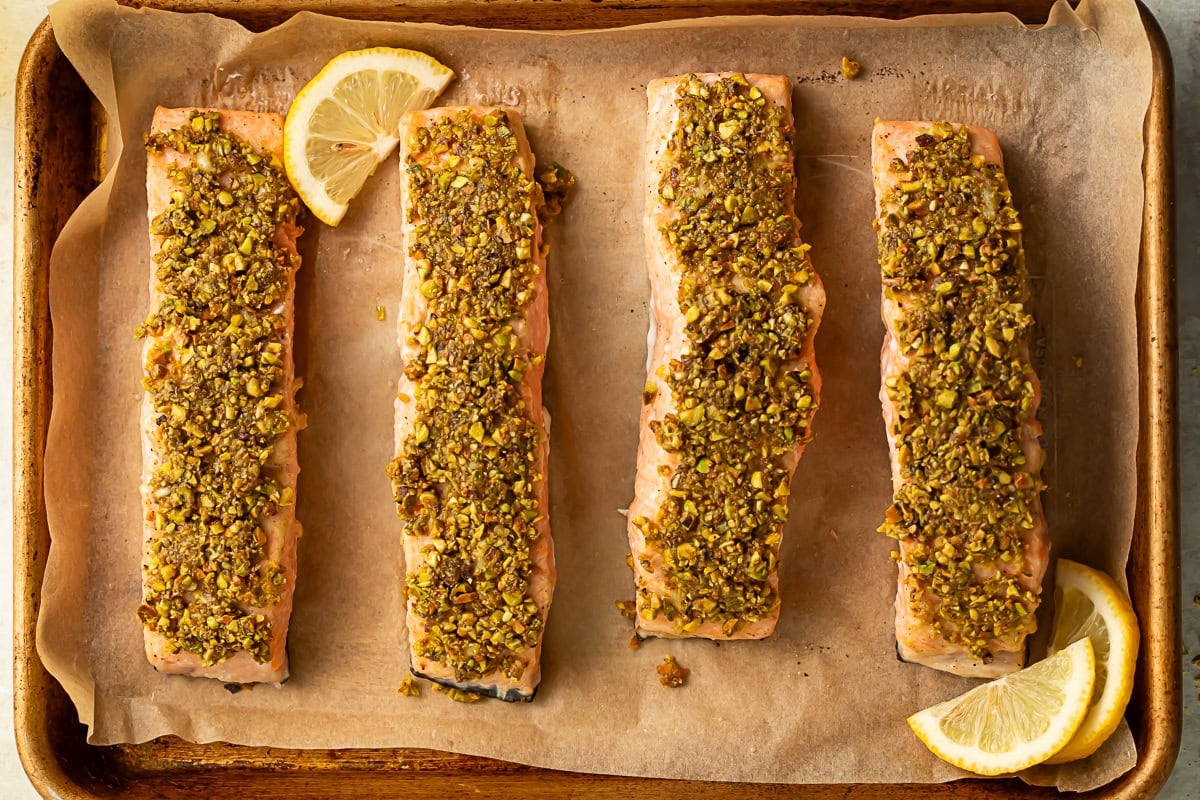 Close up of a row of pistachio crusted salmon fillets on a parchment lined baking sheet.