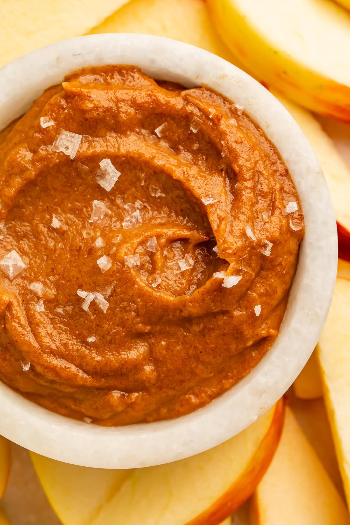 Close-up of raw salted caramel dip with flaky sea salt in a white bowl and apple slices
