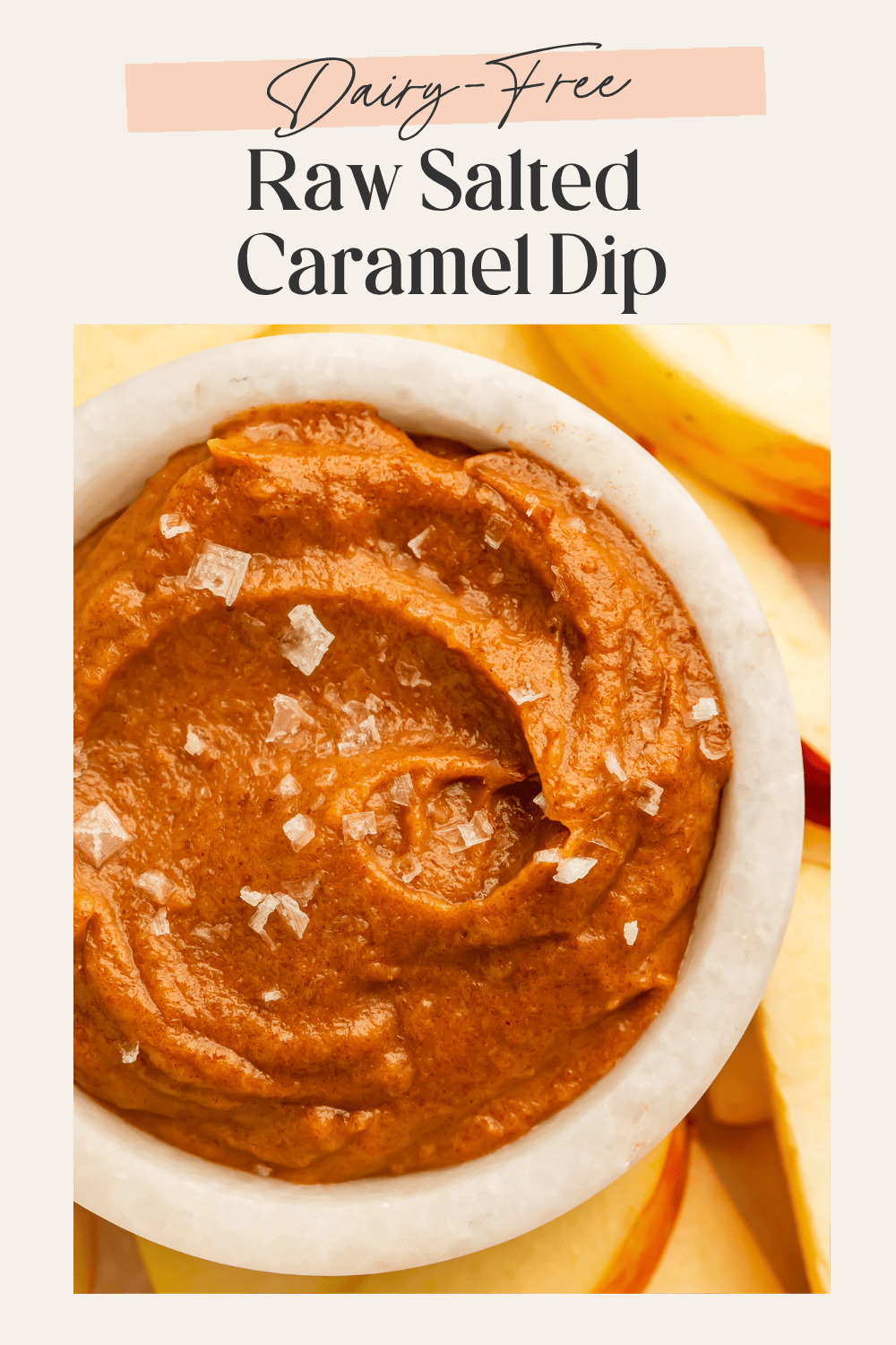 Close-up of a white marble bowl of smooth raw salted caramel dip with flaky sea salt on top surrounded by yellow apple slices