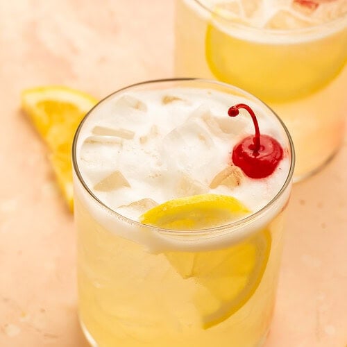 Vodka sour in a glass garnished with lemon slices and a cocktail cherry.