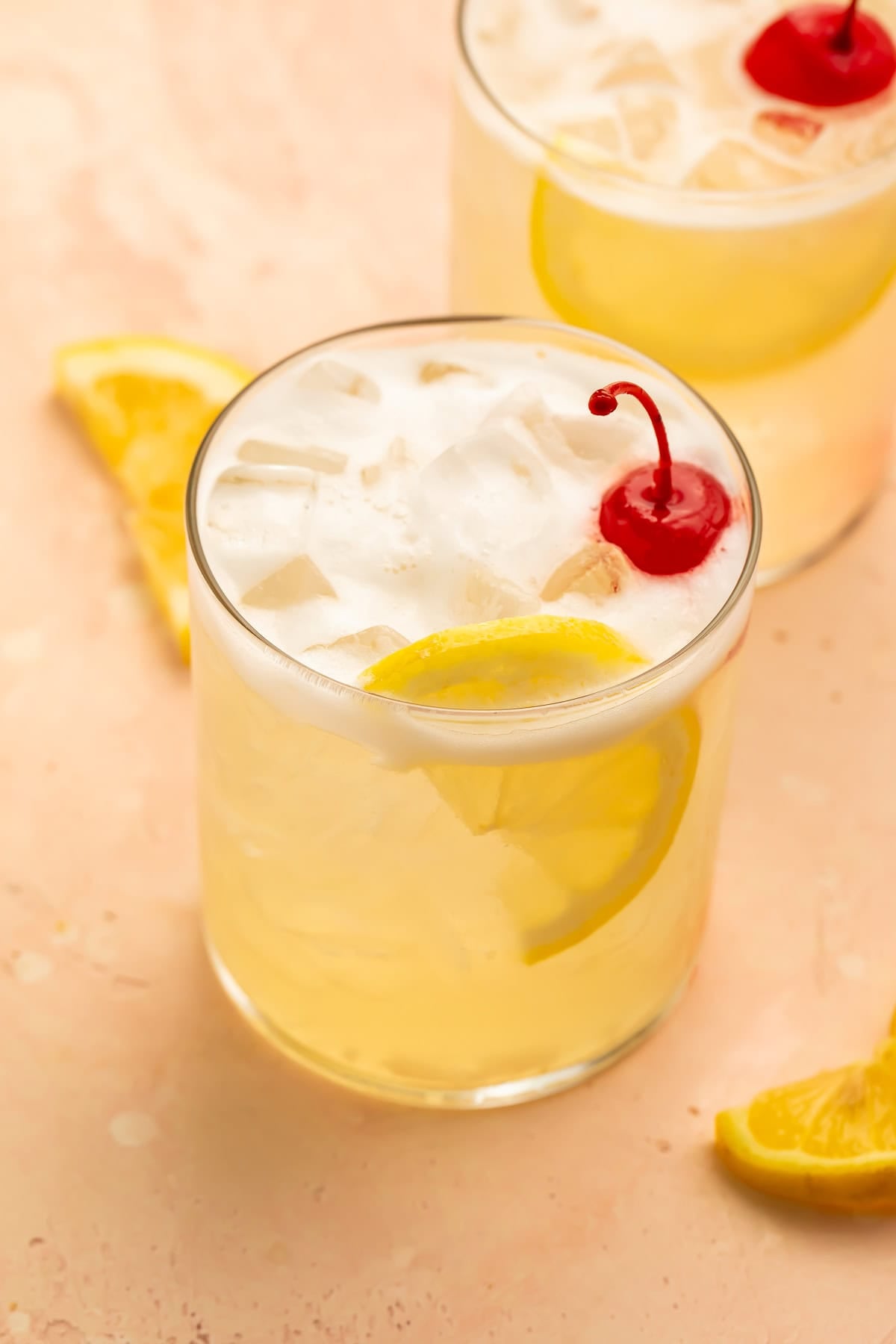 Vodka sour in a glass garnished with lemon slices and a cocktail cherry.