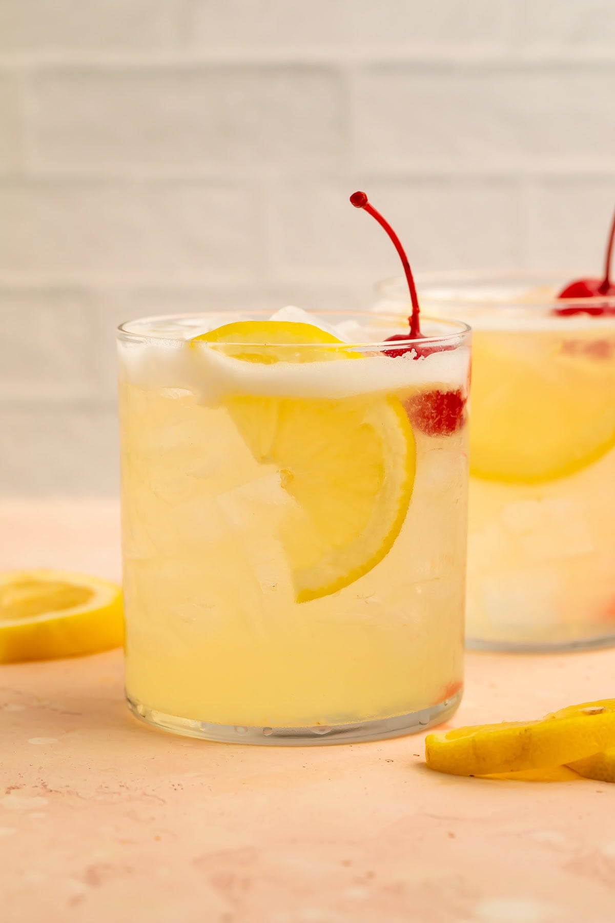 Side-on image of a pair of vodka sours with a lemon slice and cocktail cherry garnish.