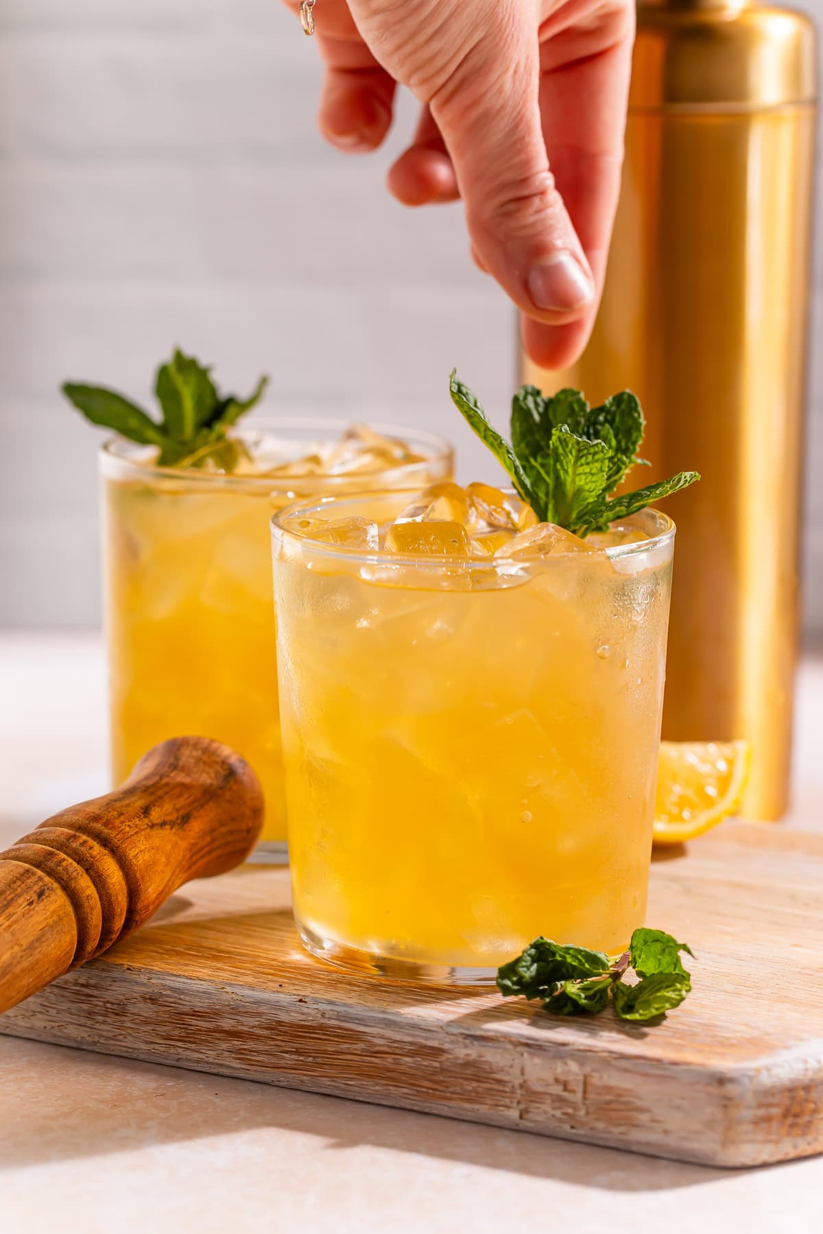 A hand adding a garnish of fresh mint to a Bourbon smash cocktail.