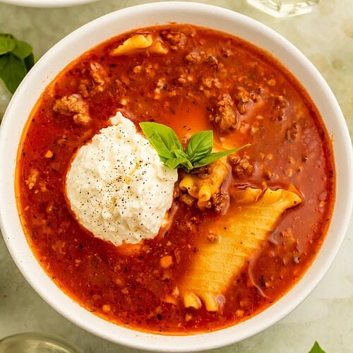 Overhead image of bowls of lasagna soup topped with scoops of ricotta. There is a glass of white wine on one side.