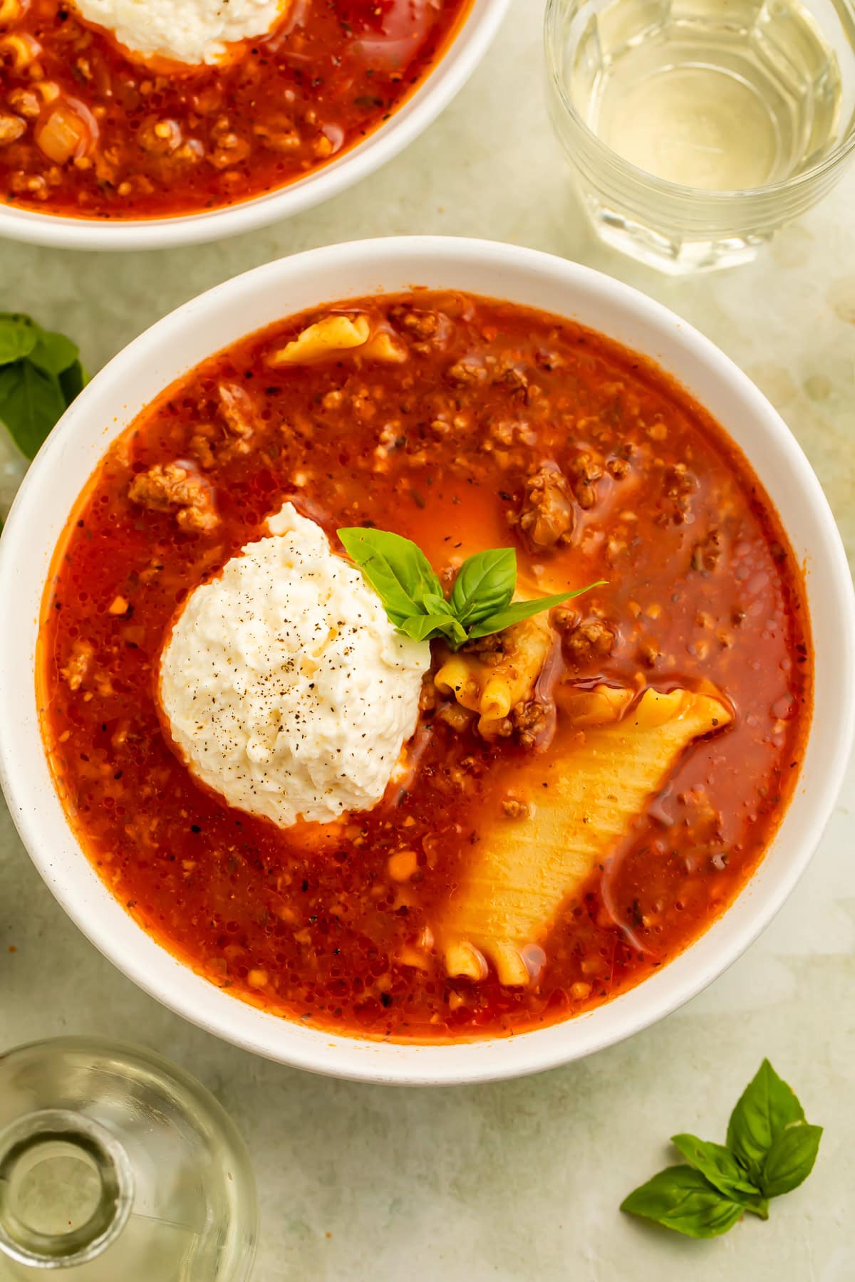 Overhead image of bowls of lasagna soup topped with scoops of ricotta. There is a glass of white wine on one side.
