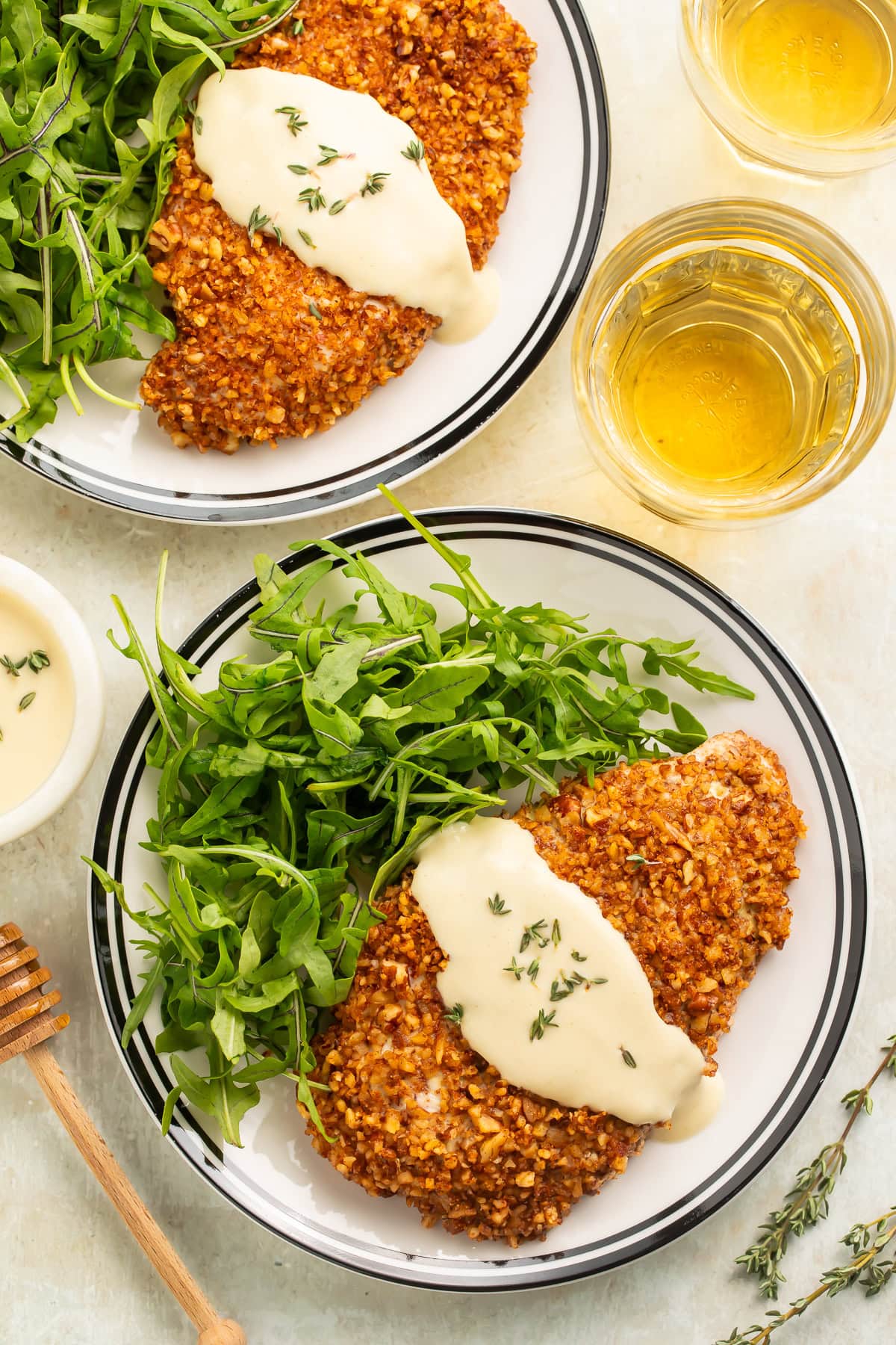 Plates of pecan chicken with a creamy sauce and a tangle of rocket pictured overhead.