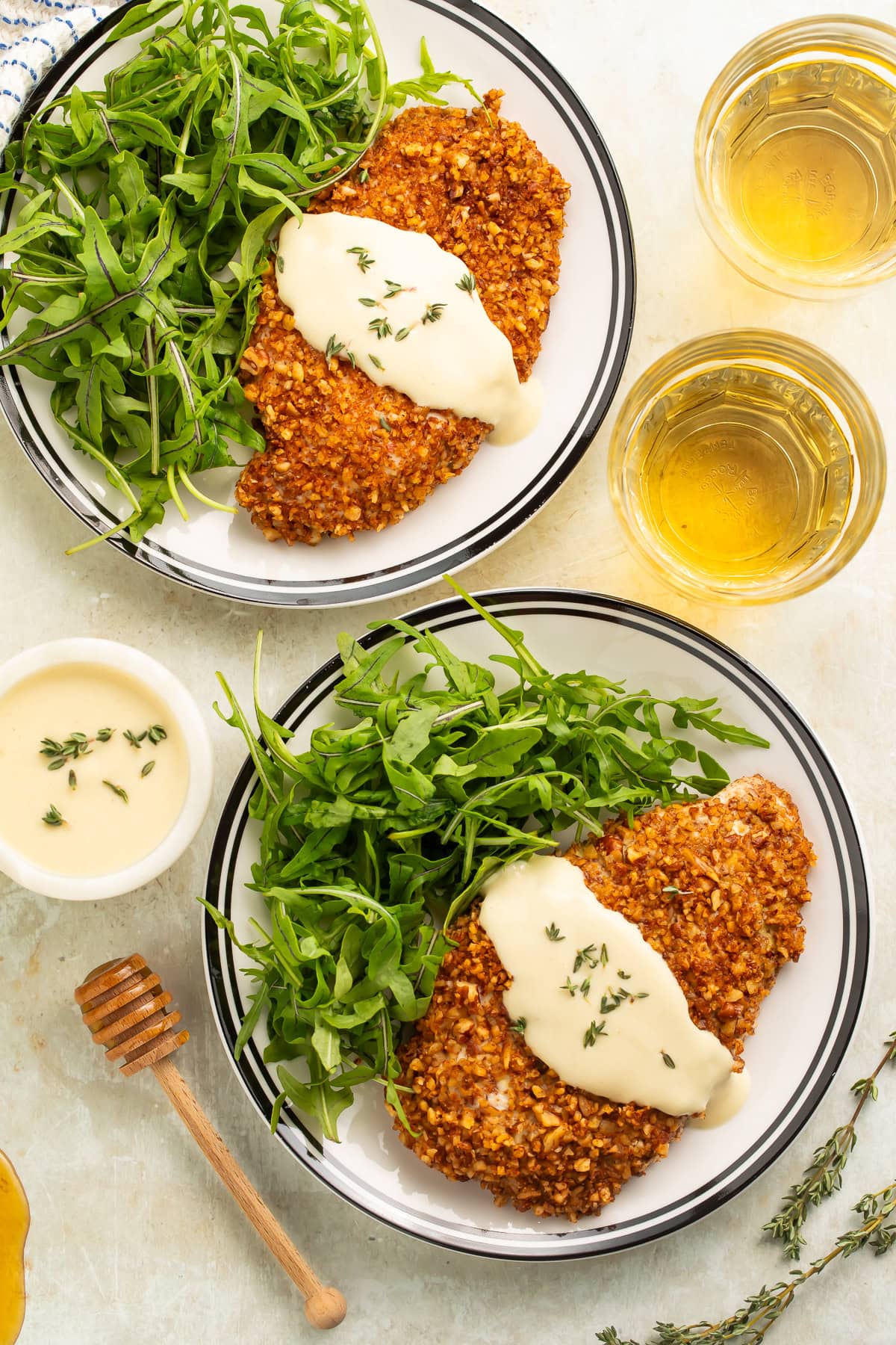 Two plates of pecan crusted chicken cutlets with a creamy sauce and arugula.