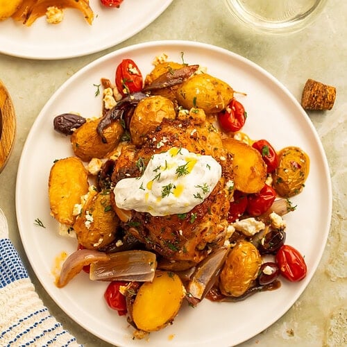 Plated up Greek sheet pan chicken and veggies, topped with a dollop of tzatziki.