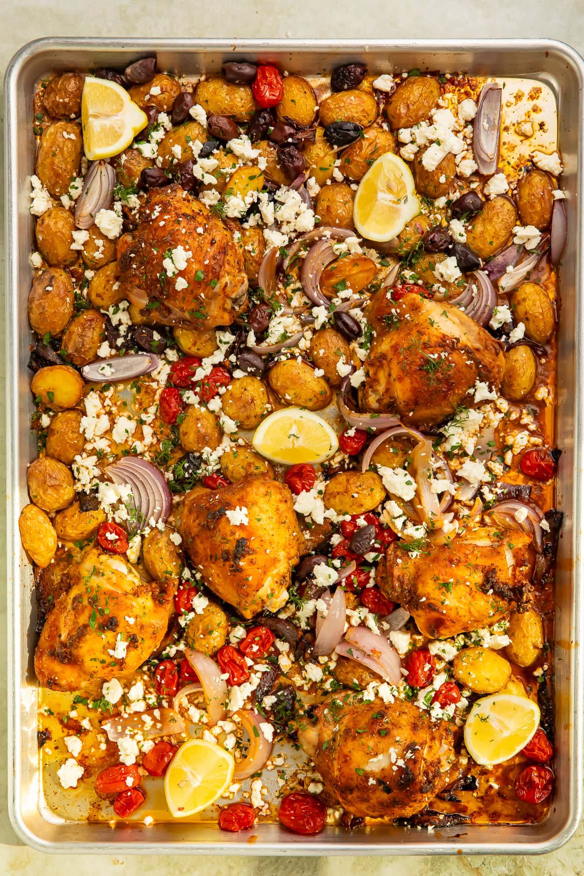 Sheet pan meal of Greek chicken thighs with roasted vegetables and feta.