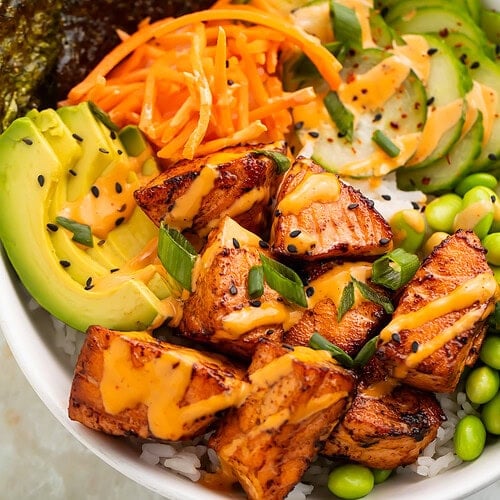 Close up of caramalised salmon bites in a rice bowl with Asian-inspired ingredients.
