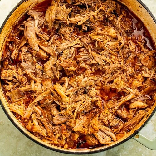 Shredded chipotle braised pork shoulder in Dutch oven with smoky braising liquid.