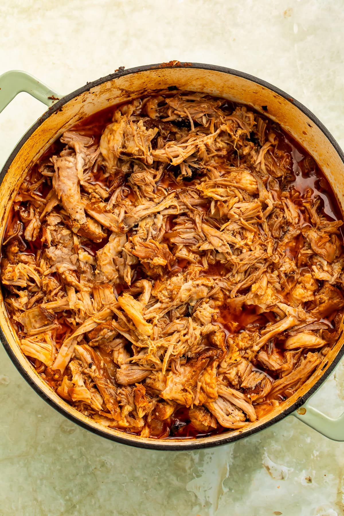 Shredded chipotle braised pork shoulder in Dutch oven with smoky braising liquid.